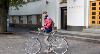 Nuori mies polkupyörän kanssa talon edessä.