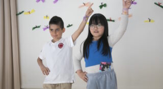 Kaksi tummahiuksista lasta seisoo toinen käsi ylhäällä