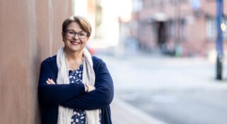 Silmälasipäinen keski-ikäinen nainen nojaa seinään kadulla