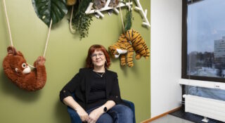 Silmälasipäinen nainen istuu seinän vieressä tuolila