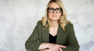 Pitkähiuksinen nainen istuu kädet ristissä vihreä paita päällä