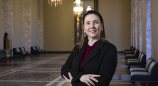 Pitkähiuksinen nainen seisoo eduskuntatalon käytävällä.