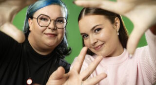 Kaksi nuorta naista vierekkäin, jotka tekevät sormilla sydämen