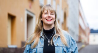 Vaaleahiuksinen nainen farkkutakissa talon edessä. Petra Malin
