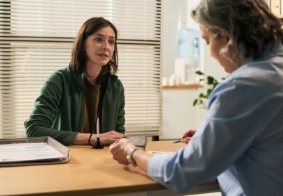 Kaksi naista keskustelee toimistomaisessa tilassa pöydän ääressä.