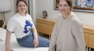 Kaksi naista nojaa työpöytään toimistolla