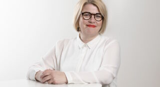 Vaaleahiuksinen nainen seisoo pöydän edessä