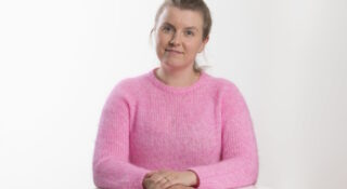 Nuori nainen pöydän ääressä vaaleanpunaisessa puserossa