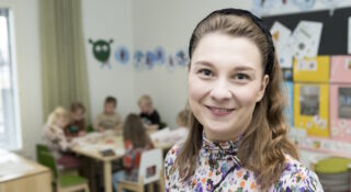 Pitkähiuksinen nainen, takana näkyy lapsia pöydän äärellä