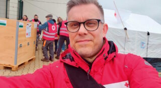 Silmälasipäinen mies punaisessa Punaisen Ristin puserossa