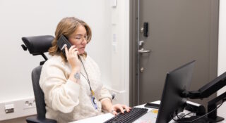 Nainen vaaleassa puserossa puhuu puhelimessa työpöydän ääressä.