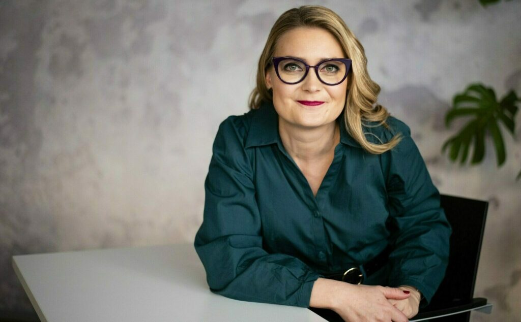 Pitkähiuksinen silmälasipäinen nainen vihreässä puserossa