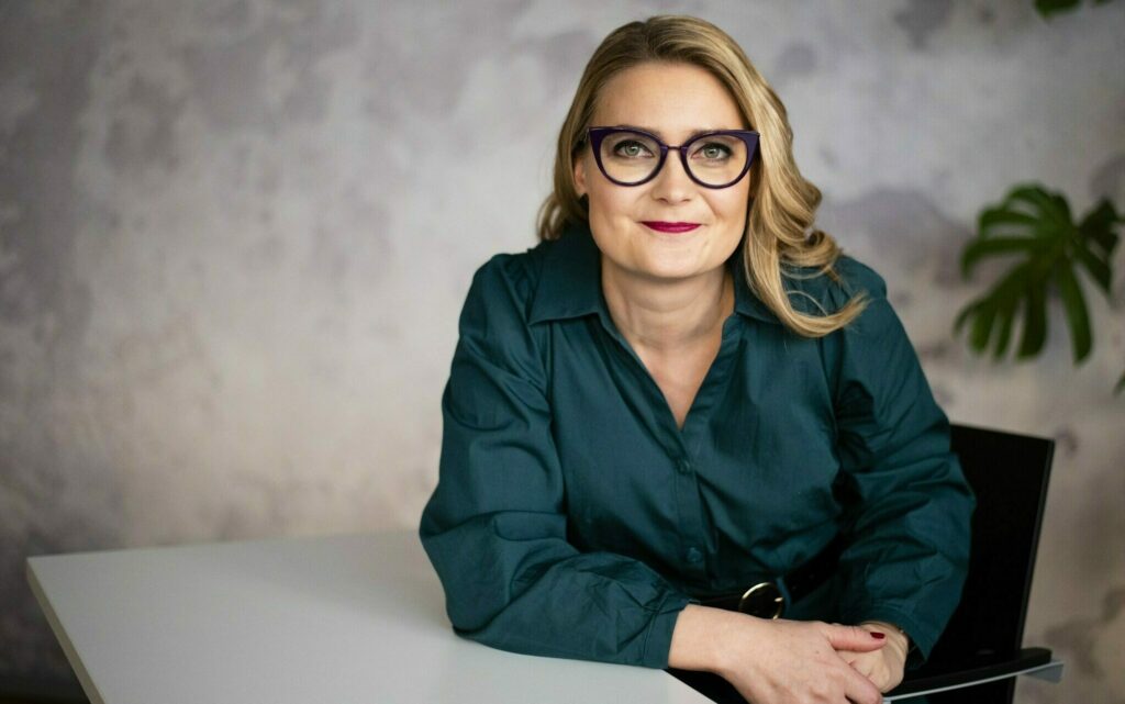 Pitkähiuksinen silmälasipäinen nainen vihreässä puserossa