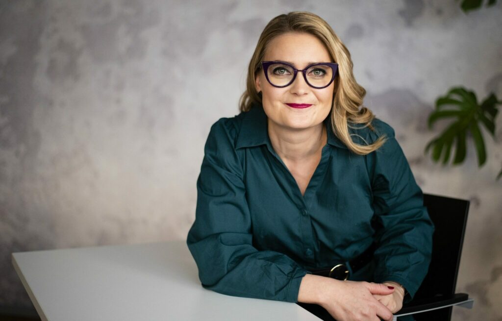 Pitkähiuksinen silmälasipäinen nainen vihreässä puserossa