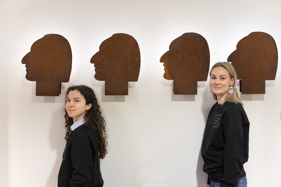 Kaksi naista seinän edessä missä pään muotoisia tauluja