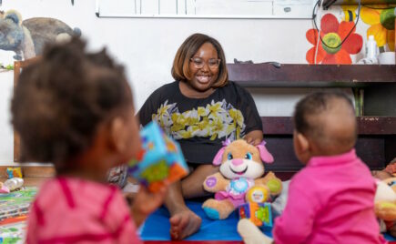 Nainen istuu lattialla lasten kanssa.