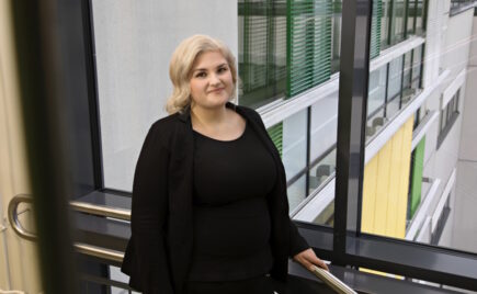 Vaaleahiuksinen nainen mustassa mekossa ikkunan edessä