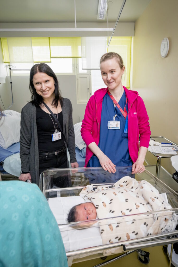 Kaksi naista ja vauva muovisessa kehdossa sairaalassa.