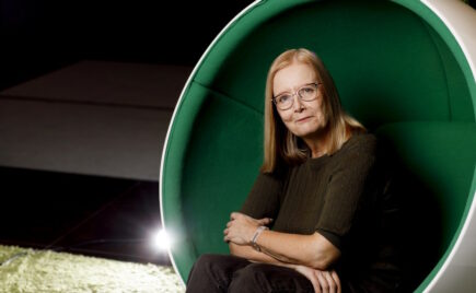 Silmälasipäinen nainen istuu vihreän taustan edessä