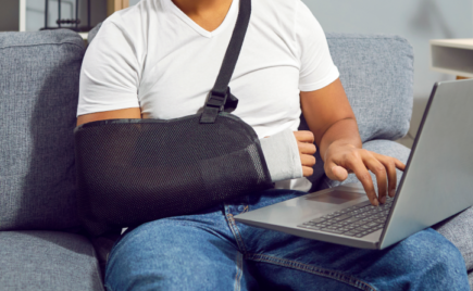 Ihminen istuu tietokoneen ääressä käsi kipsissä