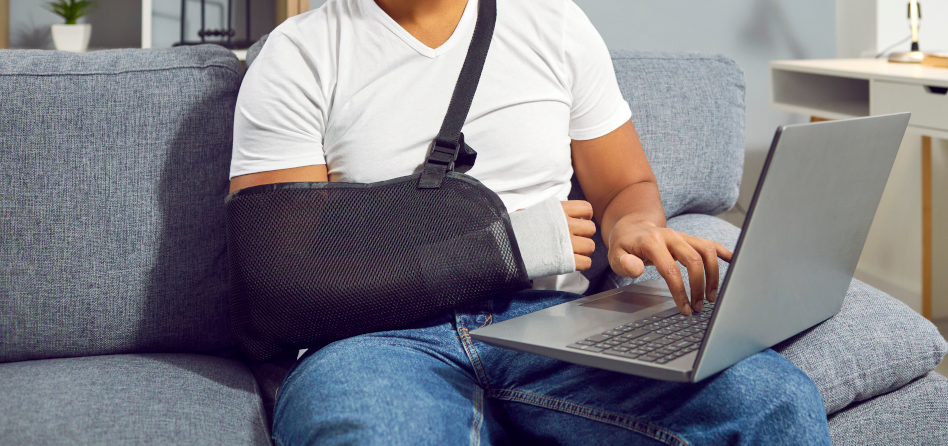 Ihminen istuu tietokoneen ääressä käsi kipsissä