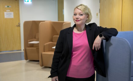 Vaaleahiuksinen nainen seisoo ja nojaa sohvaan