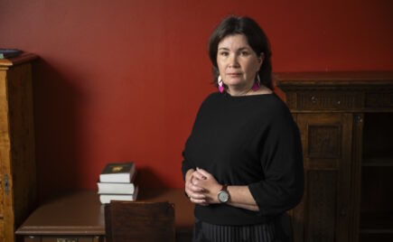 Tummatukkainen nainen seisoo punaisen seinän edessä