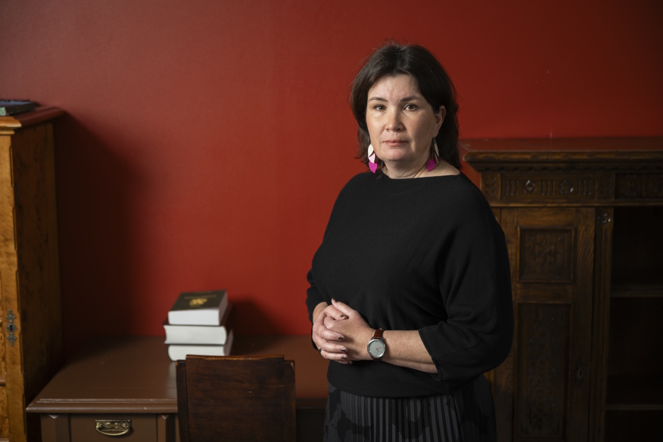 Tummatukkainen nainen seisoo punaisen seinän edessä