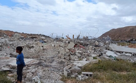 Pieni poika tuhotun rakennuksen edessä.