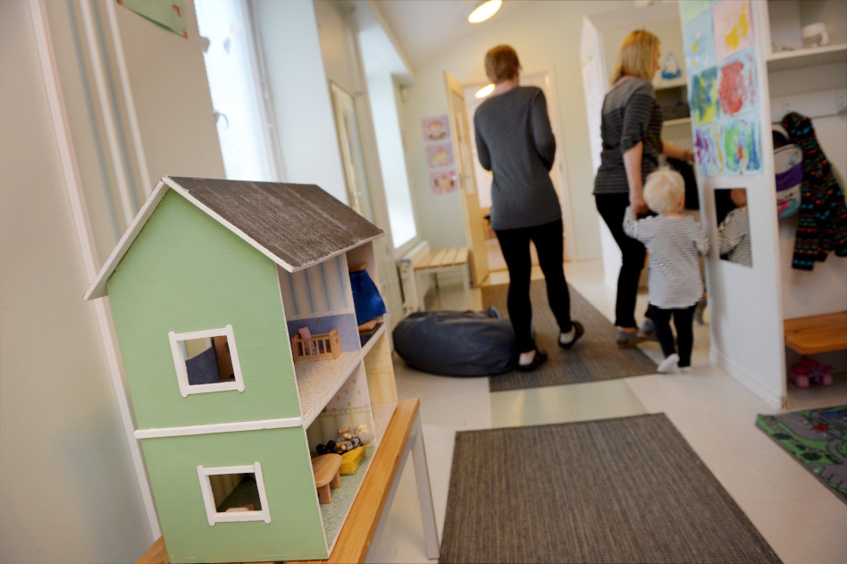 Kaksi aikuista ja lapsi päiväkodissa nukkekodin edessä
