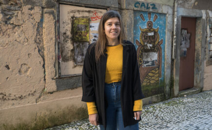 Tummahiuksinen nainen seisoo värikkään muurin edessä