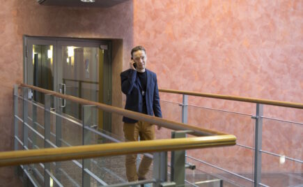 Mies sinisessä takissa puhuu puhelimeen toimistossa