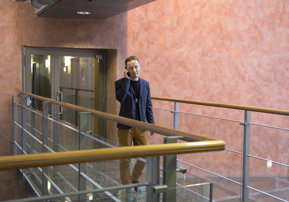 Mies sinisessä takissa puhuu puhelimeen toimistossa