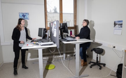 Kaksi naista seisoo vastakkain olevien työpöytien ääressä