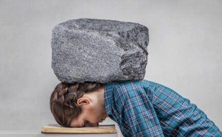 nainen nojaa päätä pöytään, pään päällä iso kivi