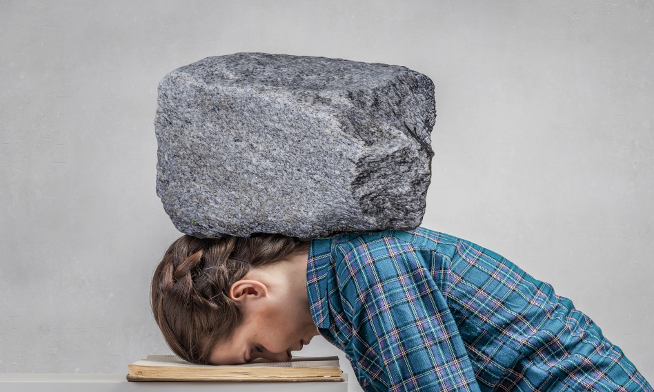 nainen nojaa päätä pöytään, pään päällä iso kivi