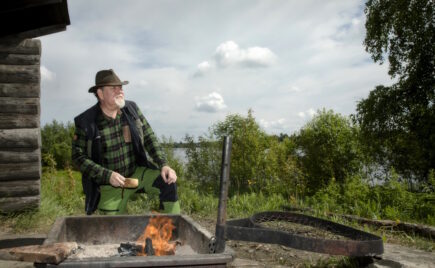 Keski-ikäinen mies metsässä nuotiotulen äärellä.