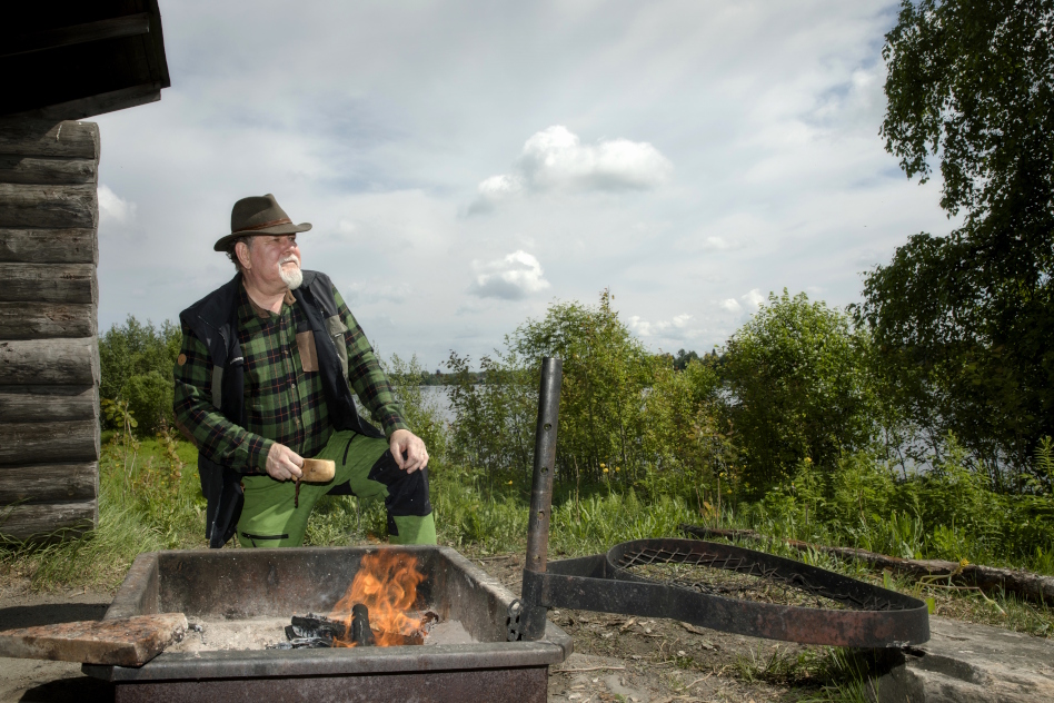 Keski-ikäinen mies metsässä nuotiotulen äärellä.