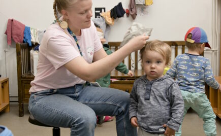 Aikuinen pukee lapselle hattua päähän päiväkodissa