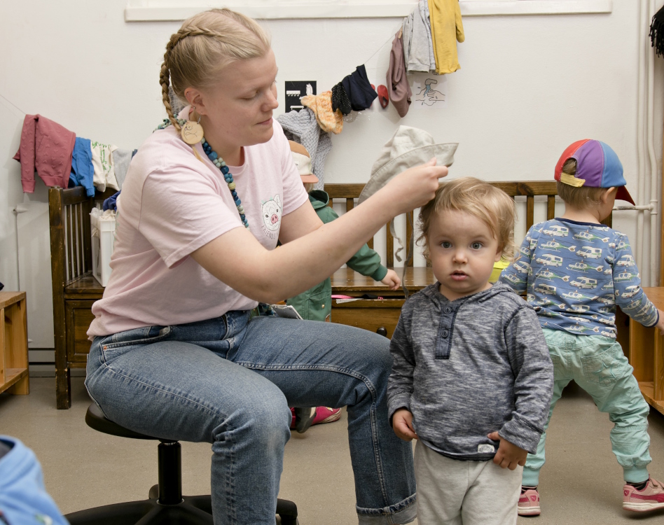 Aikuinen pukee lapselle hattua päähän päiväkodissa