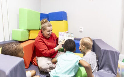 Aikuinen näyttää kuvakirjaa kahdelle lapselle