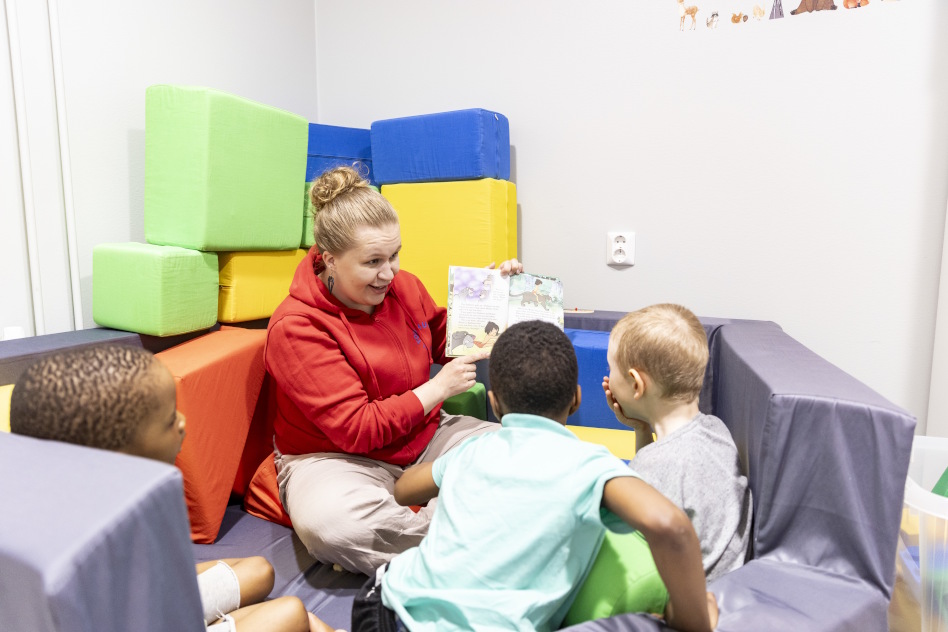 Aikuinen näyttää kuvakirjaa kahdelle lapselle