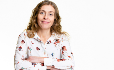 Pitkähiuksinen nainen kädet ristissä värikäs paitapusero päällä