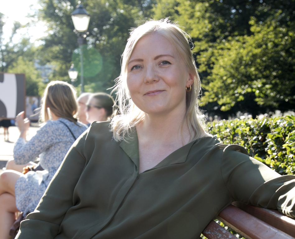 Vaaleahiuksinen nainen istuu puistonpenkillä katse kameraan päin