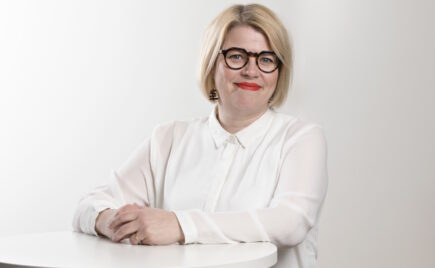 Vaaleahiuksinen nainen seisoo pöydän edessä