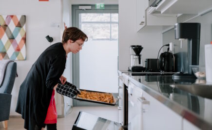 Silmälasipäinen nainen ottaa uunipellin pois uunista.