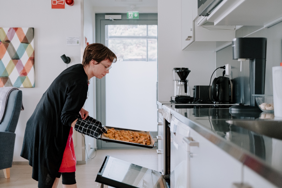 Silmälasipäinen nainen ottaa uunipellin pois uunista.