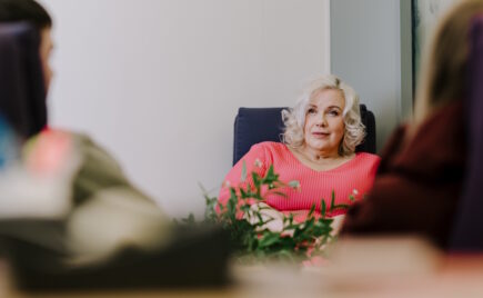 Vaaleahiuksinen nainen istuu sohvatuolilla punaisessa puserossa