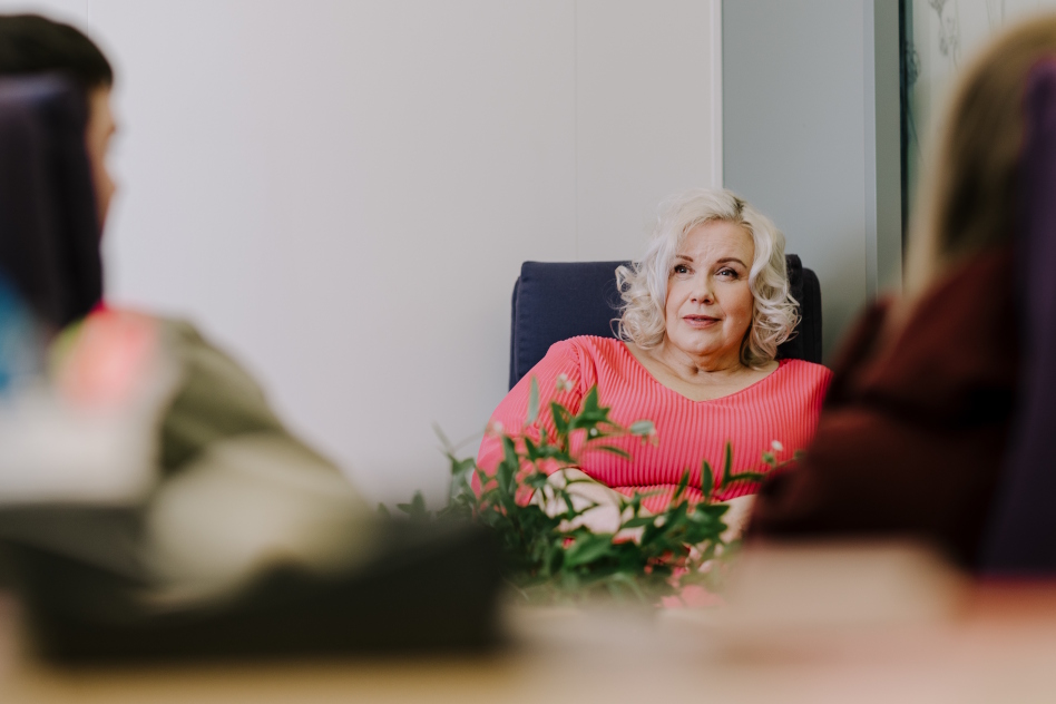 Vaaleahiuksinen nainen istuu sohvatuolilla punaisessa puserossa