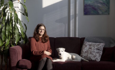 Nainen istuu sohvalla pienen, valkoisen koiran kanssa